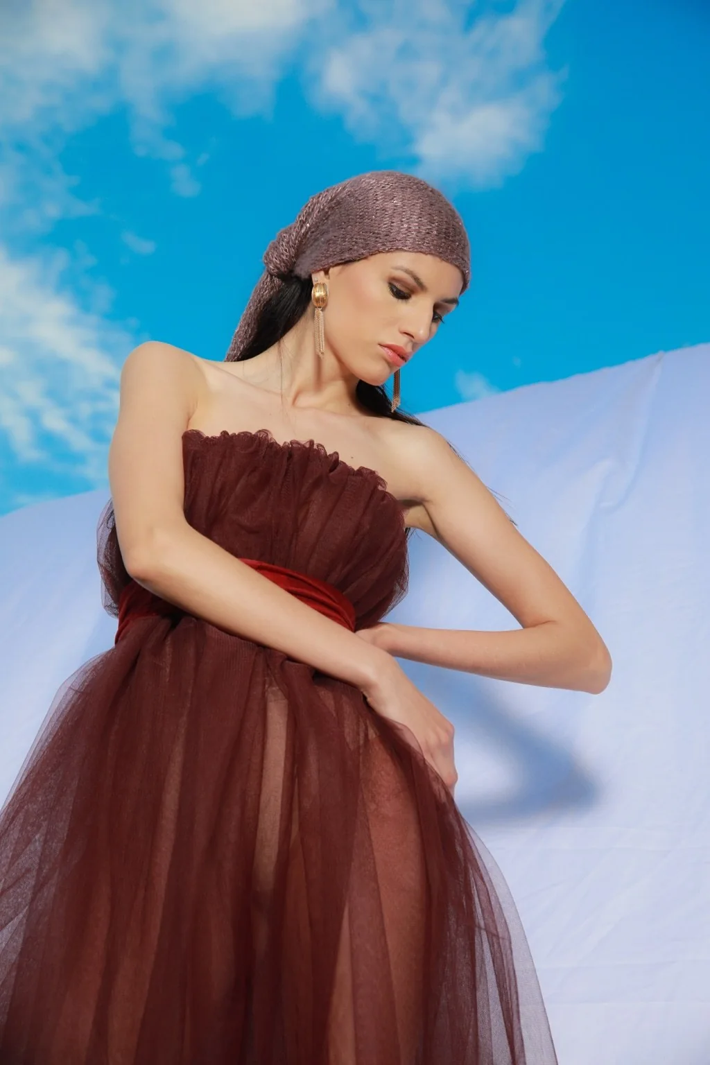 Modelo con vestido granate de tul, pañuelo y cielo azul al fondo.