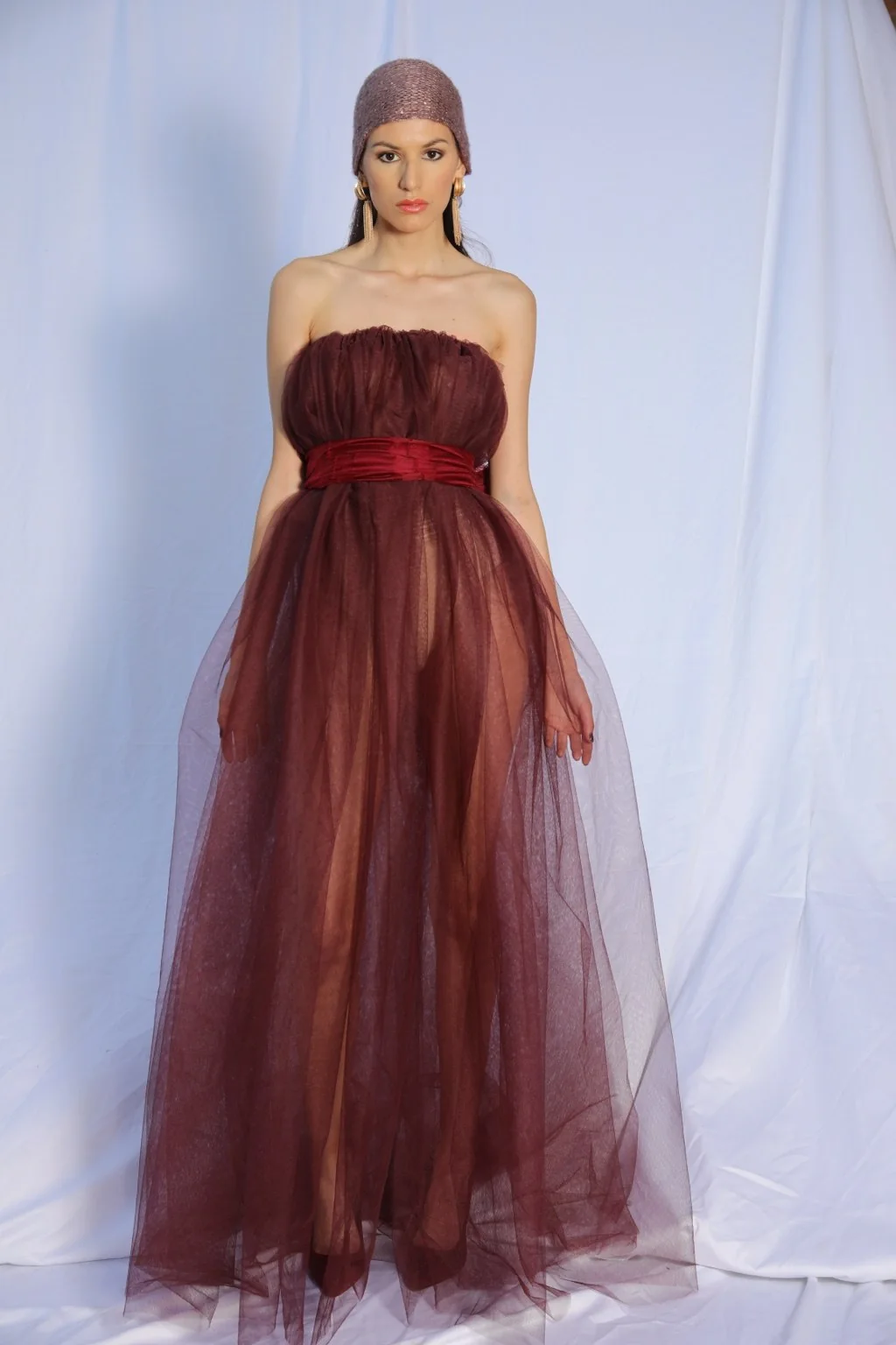 Modelo de pie con vestido granate de tul sobre fondo blanco.