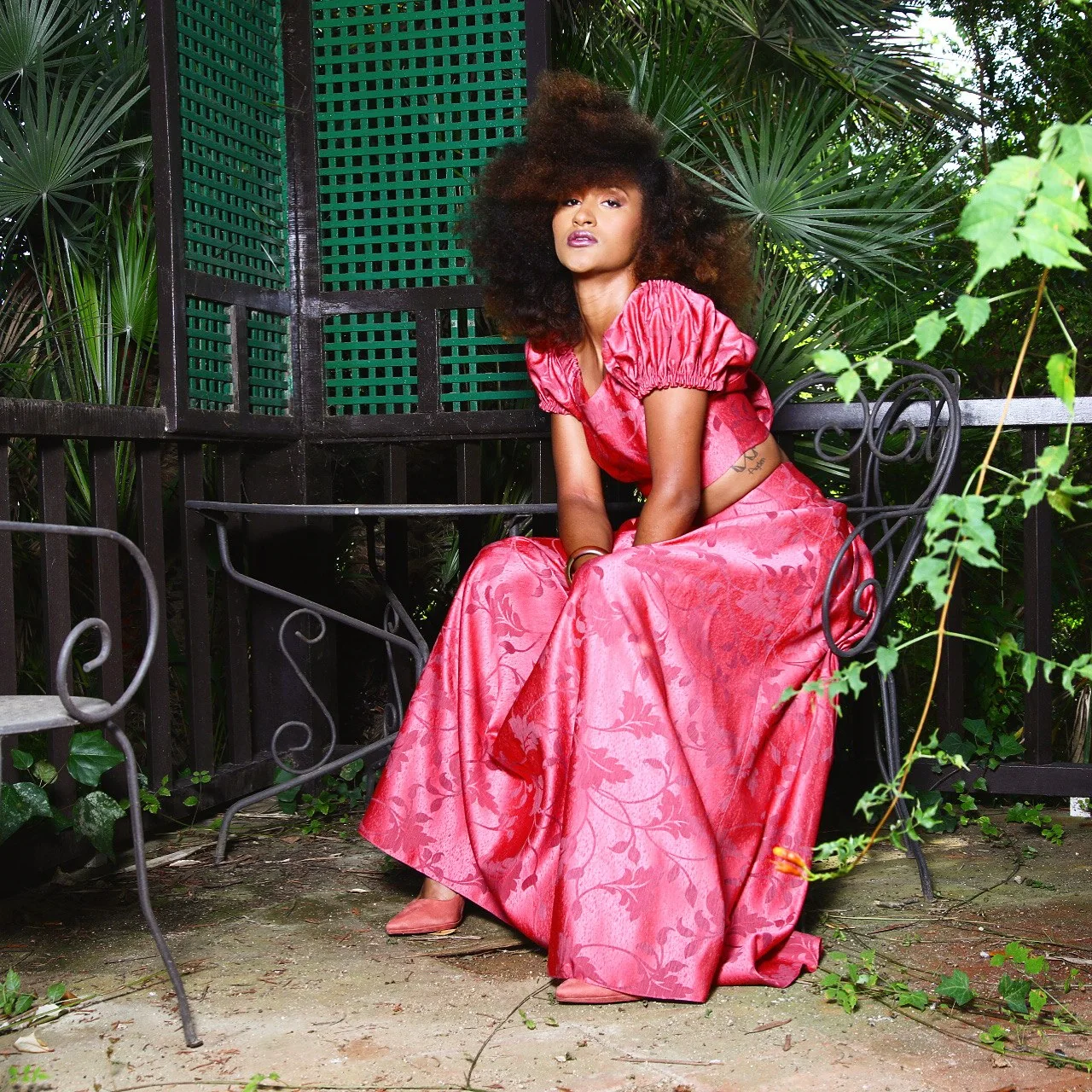 Modelo sentada con conjunto rosa entre vegetación.