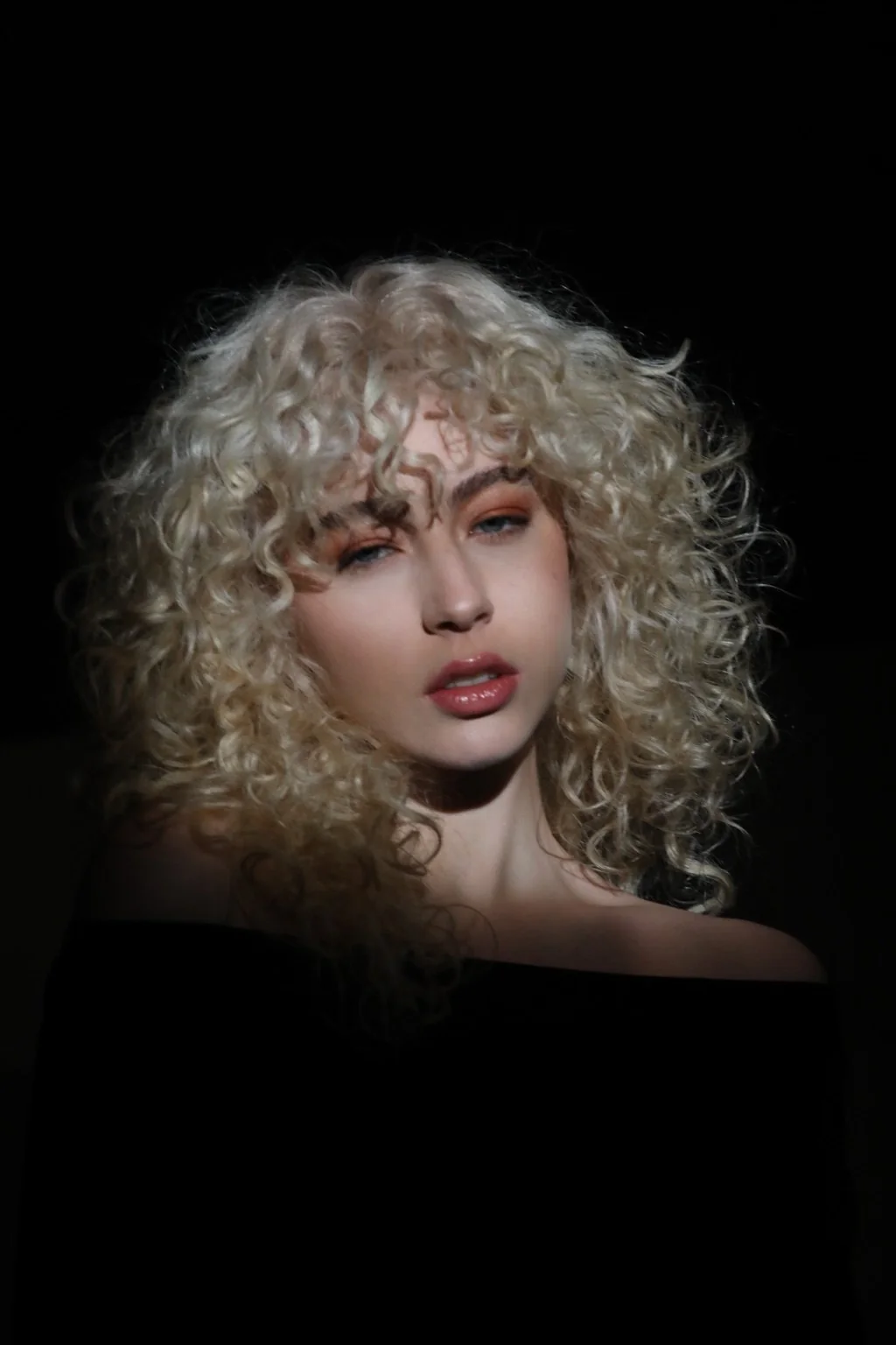 Primer plano de una modelo con cabello rizado y fondo negro.