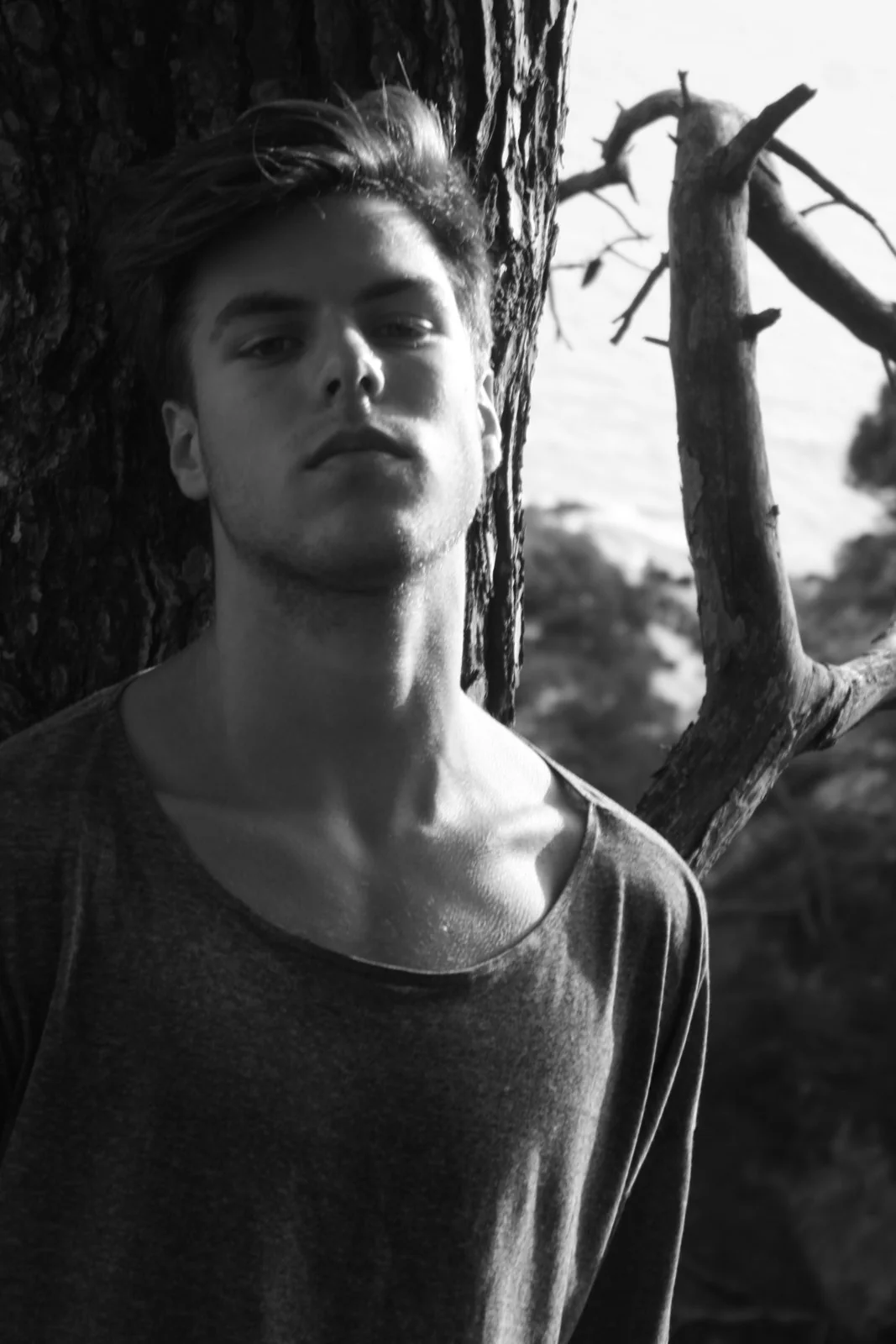 Retrato masculino en blanco y negro junto al tronco de un árbol.